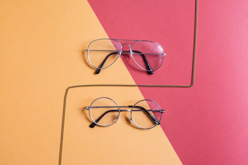 Modern eyeglasses set against a red and yellow background with fashion chain.